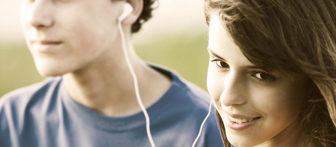 Teens sharing earphones, listening music outdoor. Summer time.  Image is captured in 12 bit RAW and processed in Adobe RGB color space.
